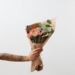 Image showing Delicate flowers living coral roses and eryngium as a beautiful bouquet in girl\'s hand with tattoo, copy space. Congratulation card.