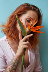 Image showing Sexy woman with tattoo holding a strelitzia flower in her hands on a blue background with copy space. Valentine\'s day card