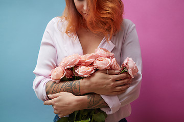 Image showing Beautiful red-haired woman with tattoo and bouquet of pink flowers on a double blue-pink background with copy space. Women\'s Day