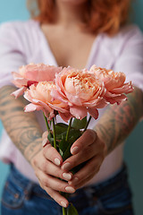 Image showing A woman with a tattoo holding delicate pink roses in her hands on a blue background with copy space for text. Holiday gift