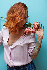 Image showing Sexual girl with ginger hair and flowers living coral color in her hands with tattoo on a blue background, copy space. Gift on Woman\'s, Mother\'s Day.