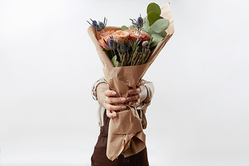 Image showing Lady\'s hands hold a nice bouquet from fresh fragrant flowers living coral colored roses on a light background. Copy space. Greeting card for Mother\'s Day.