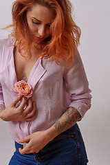 Image showing Sexual red-haired girl with fresh flower living coral color in hands with tattoo on a gray background. Copy space. Gift on Woman\'s or Mother\'s Day.