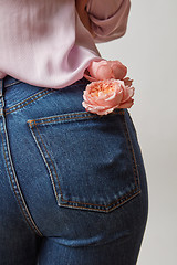 Image showing Woman wearing of jean pants and pink shirt from back with fresh flowers in a pocket on a gray background, copy space.