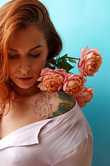 Image showing Attractive girl with tattoo on her shoulders and bouquet of coral roses on a blue background, place for text. A gift for Mother\'s Day.