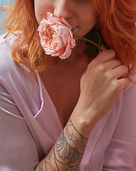 Image showing Smiling happy red-haired girl in a pink shirt and delicate rose in her hand with tattoo copy space. Close-up. The gift for Mother\'s Day.