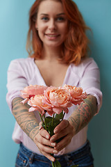 Image showing A smiling girl with a tattoo gives a bouquet of pink roses around a blue background with copy space. Mother\'s Day Gift