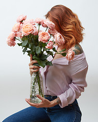 Image showing Red-haired girl with a tattoo and a beautiful pink bouquet of roses in a vase on a gray background with copy space. Mothers Day.