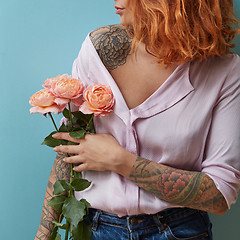 Image showing A young woman with a tattoo holds in her hand a bouquet of pink roses around a blue background with copy space. Mother\'s day concept