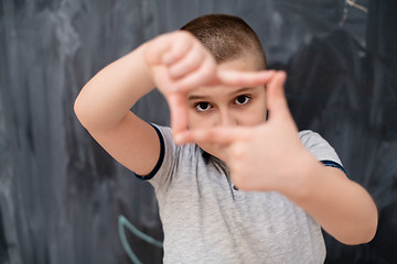 Image showing happy boy making hand frame gesture in front of chalkboard