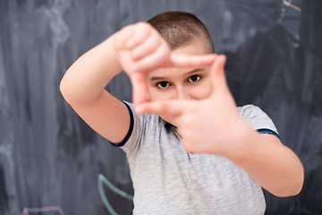 Image showing happy boy making hand frame gesture in front of chalkboard