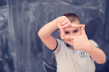 Image showing happy boy making hand frame gesture in front of chalkboard