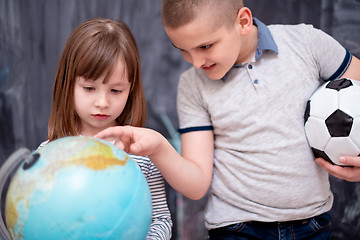 Image showing boy and little girl using globe of earth in front of chalkboard