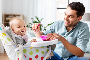 Image showing father feeding happy baby in highchair at home