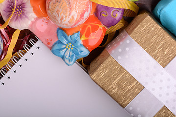 Image showing Arrangement of Gift Boxes in Wrapping Paper with Checkered Ribbons and Decorated Easter Eggs. White paper notepad