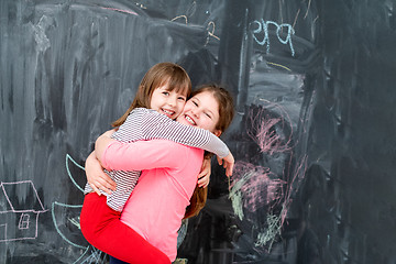 Image showing little girls hugging in front of chalkboard