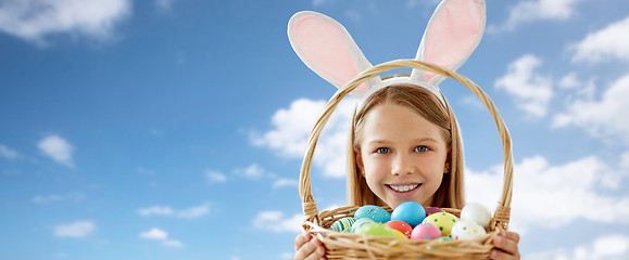 Image showing happy girl with easter eggs in basket over sky