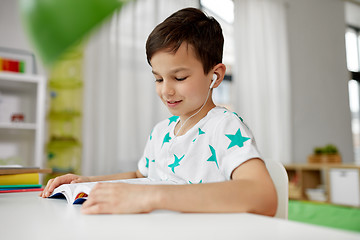 Image showing student boy in earphones reading book at home