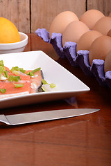 Image showing fresh salmon fillet close up on white plate. knife, eggs and lemon