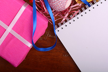 Image showing Arrangement of Gift Boxes in Wrapping Paper with Checkered Ribbons and Decorated Easter Eggs. White paper notepad