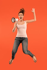 Image showing Beautiful young woman jumping with megaphone isolated over red background