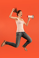 Image showing Beautiful young woman jumping with megaphone isolated over red background