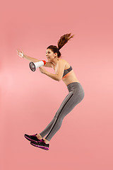 Image showing Beautiful young woman jumping with megaphone isolated over red background