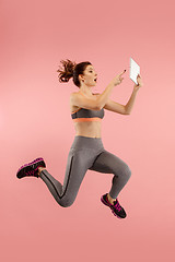 Image showing Image of young woman over blue background using laptop computer or tablet gadget while jumping.