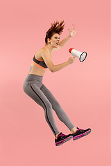 Image showing Beautiful young woman jumping with megaphone isolated over red background