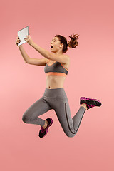 Image showing Image of young woman over blue background using laptop computer or tablet gadget while jumping.