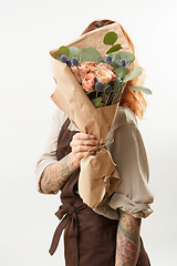 Image showing Girl with red hair hide her face big fresh bunch from natural roses and green leaves on a light background. Copy space. Congratulation card.