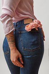 Image showing Young pretty woman dressed in blue jeans and pink jacket with fresh roses in a back pocket and her hand tattoo on a gray background, copy space.