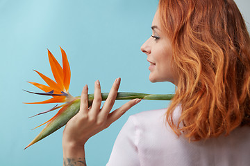 Image showing Exotic flower strelitzia decorates shoulder smiling woman on a blue background with copy space. Postcard layout