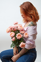 Image showing A vase with a bouquet of pink roses is being held by a girl with a tattoo around a gray background with space for text. Present