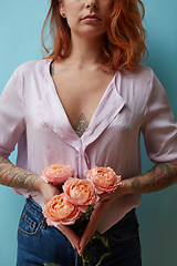 Image showing Sexy girl with tattoo holding a bouquet of pink roses on a blue background with copy space. Creative layout for postcards