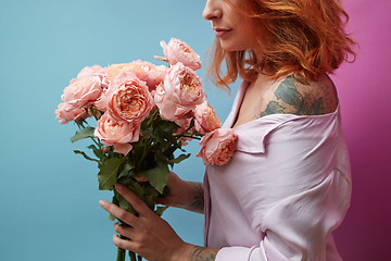 Image showing Gentle pink roses in the hands of a girl with a tattoo on a double pink blue background with copy space for text. Birthday present