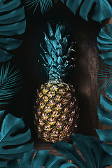 Image showing Fresh pineapple on an old wooden background decorated with a frame of palm leaves. Tropical fruit