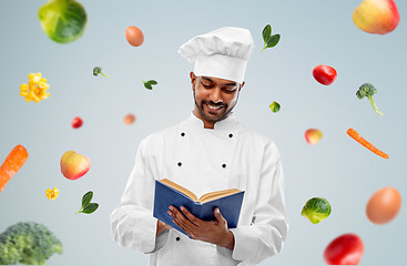 Image showing happy indian chef reading cookbook over vegetables