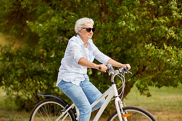 Image showing happy senior woman riding bicycle at summer park