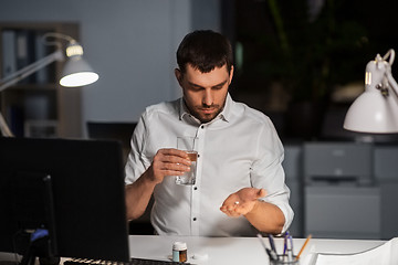 Image showing businessman taking medicine pills at night office