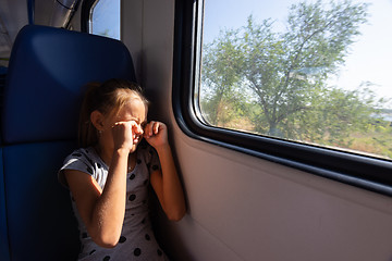 Image showing A girl rubs her eyes from the sun in an electric train car