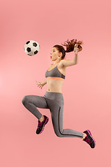 Image showing Forward to the victory.The young woman as soccer football player jumping and kicking the ball at studio on a red