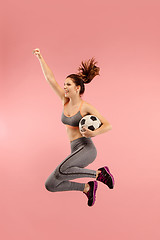 Image showing Forward to the victory.The young woman as soccer football player jumping and kicking the ball at studio on a red