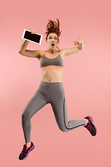 Image showing Image of young woman over blue background using laptop computer or tablet gadget while jumping.