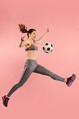 Image showing Forward to the victory.The young woman as soccer football player jumping and kicking the ball at studio on a red