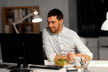 Image showing businessman at computer eating at night office