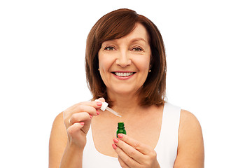 Image showing smiling senior woman with bottle of serum