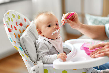 Image showing father feeding baby sitting in highchair at home