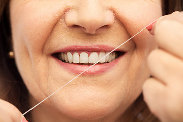 Image showing senior woman cleaning her teeth by dental floss