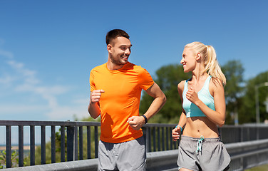 Image showing couple with fitness trackers running along bridge